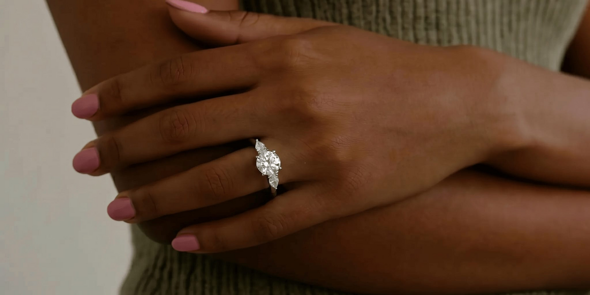 Lab-grown diamond round engagement ring with petite side stones, worn on a woman's hand