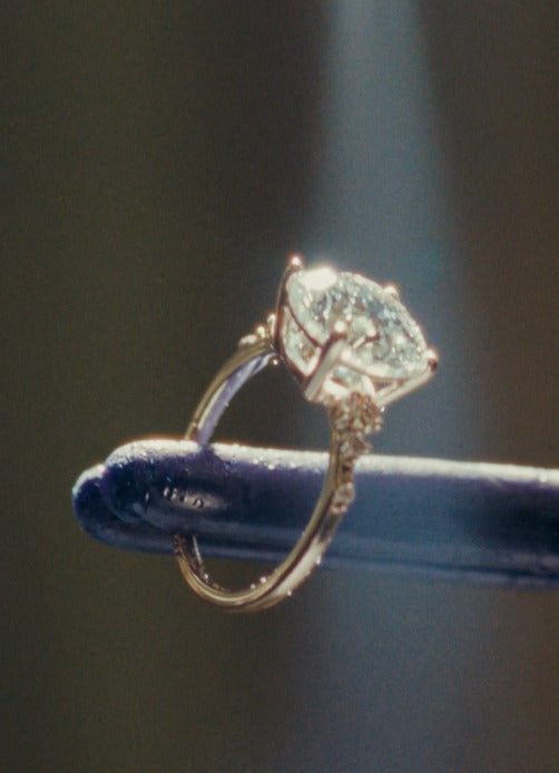 Diamond engagement ring with side accents held on a jeweler's tool under light