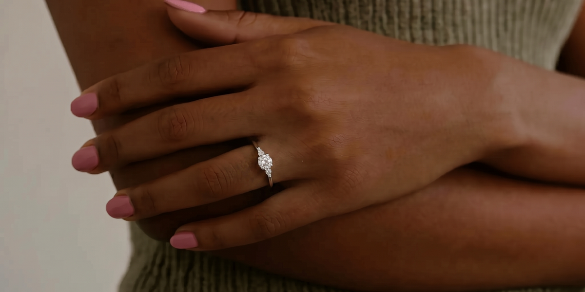 Mined diamond round engagement ring with petite side stones, worn on a woman's hand