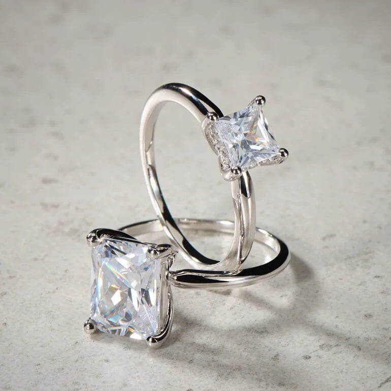 Two princess cut solitaire engagement rings with a thin band by Spence Diamonds