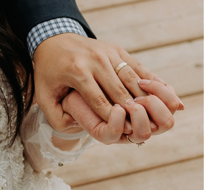 Groom wearing a gold wedding band, holding his bride's ringed hand