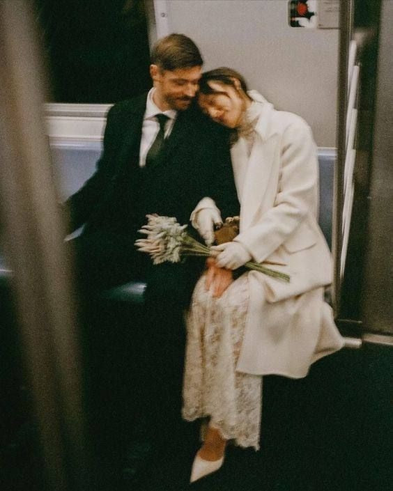 Just married couple sitting together on a train, bride holding flowers.