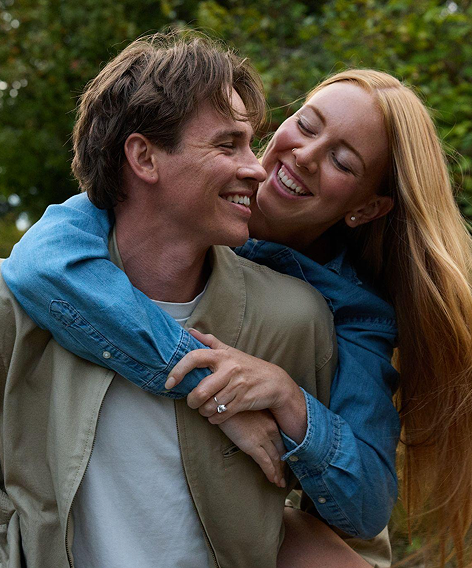Smiling woman hugs her partner from behind, her engagement ring on show