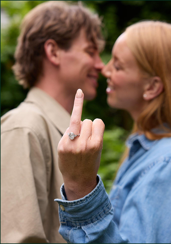 Portrait image of woman shows her oval engagement ring to the camera